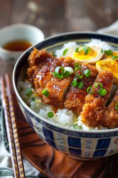 a bowl filled with rice and meat on top of a wooden table next to chopsticks