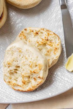 two english muffins on a white plate with butter and a knife next to them