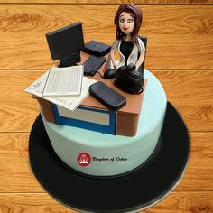 a cake with a woman sitting on top of a desk and laptop computer next to it