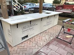 an outdoor bar is being built on the side of a brick patio with cars parked in the background