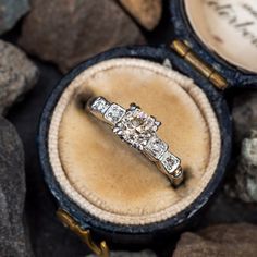 an engagement ring sits in its box on some rocks