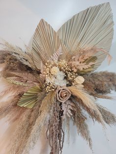 an arrangement of dried flowers and feathers on a wall