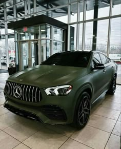 a green mercedes suv is parked in front of a glass building with large windows and doors