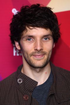 a close up of a person wearing a brown shirt and black jacket with a red background