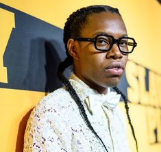 a woman with glasses and braids standing in front of a yellow wall wearing a bow tie