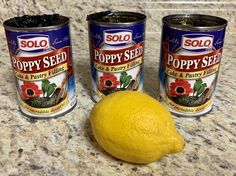 three cans of poppy seed and a lemon on a granite countertop with a yellow fruit