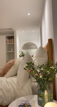 a vase with flowers sitting on top of a table in front of a white bed