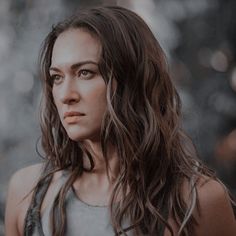 a woman with long brown hair wearing a gray tank top and looking off into the distance