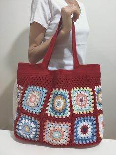 a woman holding a red crocheted bag on top of a white table next to a wall