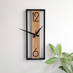 a wooden clock on the wall with numbers and numerals is displayed next to a potted plant