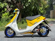 a yellow and white scooter parked on the side of a road next to trees