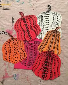 four pieces of crocheted pumpkins are on a sheet of paper with paint splatters all over them