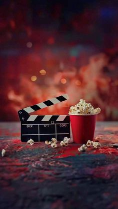 a red cup filled with popcorn sitting next to a movie clapper on top of a table