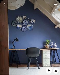 a chair and desk in front of a blue wall with plates hanging on the wall