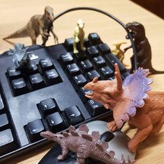 toy dinosaurs sitting on top of a computer keyboard next to a mouse and keyboard pad