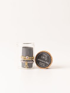 a small jar filled with black and gold bracelets next to a round glass container