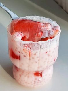 a spoon in a cup filled with ice cream and strawberries on top of a table