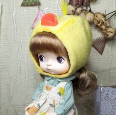 a doll wearing a yellow hat and dress with feathers on it's head, standing next to a wall