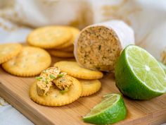 limes and crackers on a wooden cutting board with some sort of food in the background