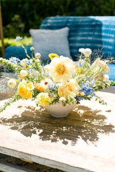 a bowl filled with flowers sitting on top of a wooden table next to a blue couch