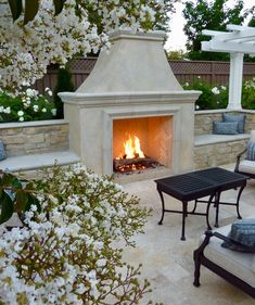 an outdoor fireplace in the middle of a patio with seating around it and white flowers