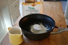 a pan with flour in it next to a cup on a counter top, and a bag of organic all purpose flour