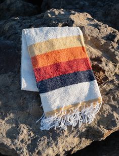 an orange, yellow and blue striped towel on top of a rocky surface next to some rocks