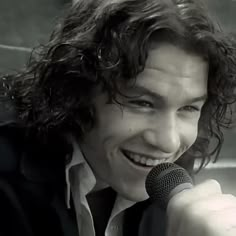 a man with long hair holding a microphone in his right hand and smiling at the camera