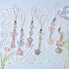 several charms are hanging on a lace doily with flowers in the foreground and a small pink flower to the side