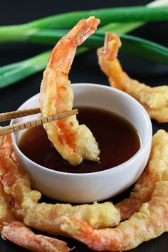 shrimp sticks being dipped with dipping sauce in a small white bowl on a black surface