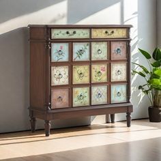 a wooden cabinet with multicolored tiles on the doors and drawers in front of a potted plant