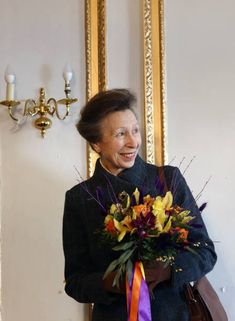 an older woman holding a bouquet of flowers in front of a wall with paintings on it