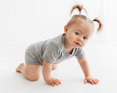 a baby crawling on the ground wearing a gray shirt and grey shorts with two ponytails