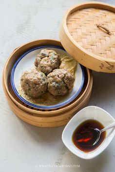 some meatballs are sitting on a plate next to a bowl of dipping sauce and a bamboo basket