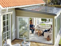 two people sitting on chairs in a small patio area with sliding glass doors and an orange roof