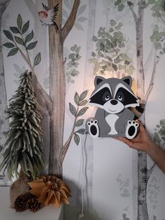 a person holding up a raccoon cutout in front of a forest scene