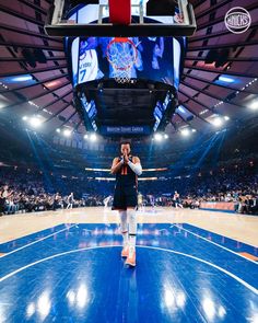 a man standing on top of a basketball court in front of a large screen tv