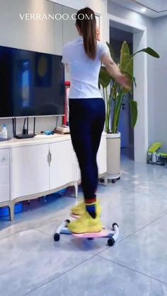 a woman is riding on a skateboard in the living room with a plant behind her