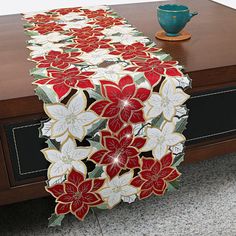 a table runner with red and white poinsettis on it next to a blue vase