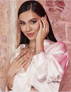 a woman with long hair wearing a white dress and holding her hand up to her face