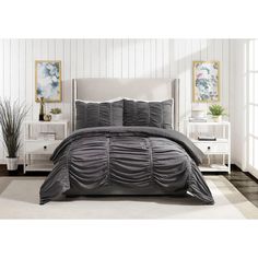 a bed with grey comforter and pillows in a white room next to two nightstands