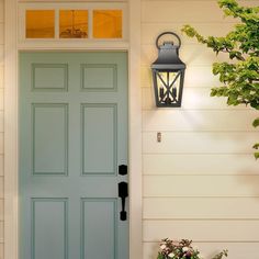 a blue front door with a light on it and potted plants in the foreground