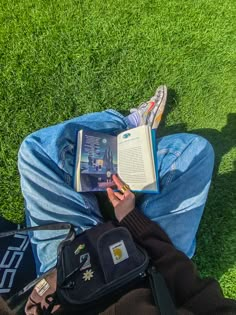 a person laying on the grass reading a book and holding a cell phone in their hand