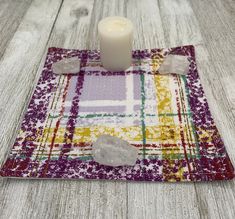 a white candle sitting on top of a table next to rocks and a plaid cloth