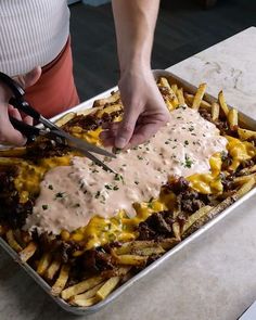 a person cutting up some food on top of a pan filled with fries and gravy