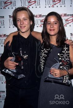 two people standing next to each other holding trophies