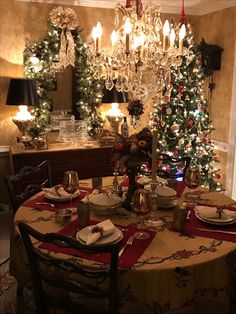 a dining room table set for christmas dinner with a tree in the corner and lights on