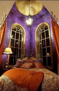 a bedroom with purple walls and two arched windows in the corner, along with an orange bed spread