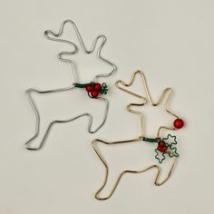 two metal reindeer ornaments with holly berries on them, one is red and the other is silver