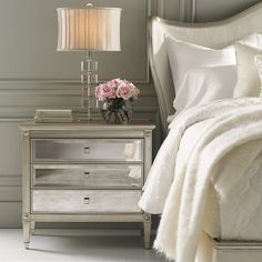 a white bed sitting next to a silver nightstand with flowers on it and a lamp